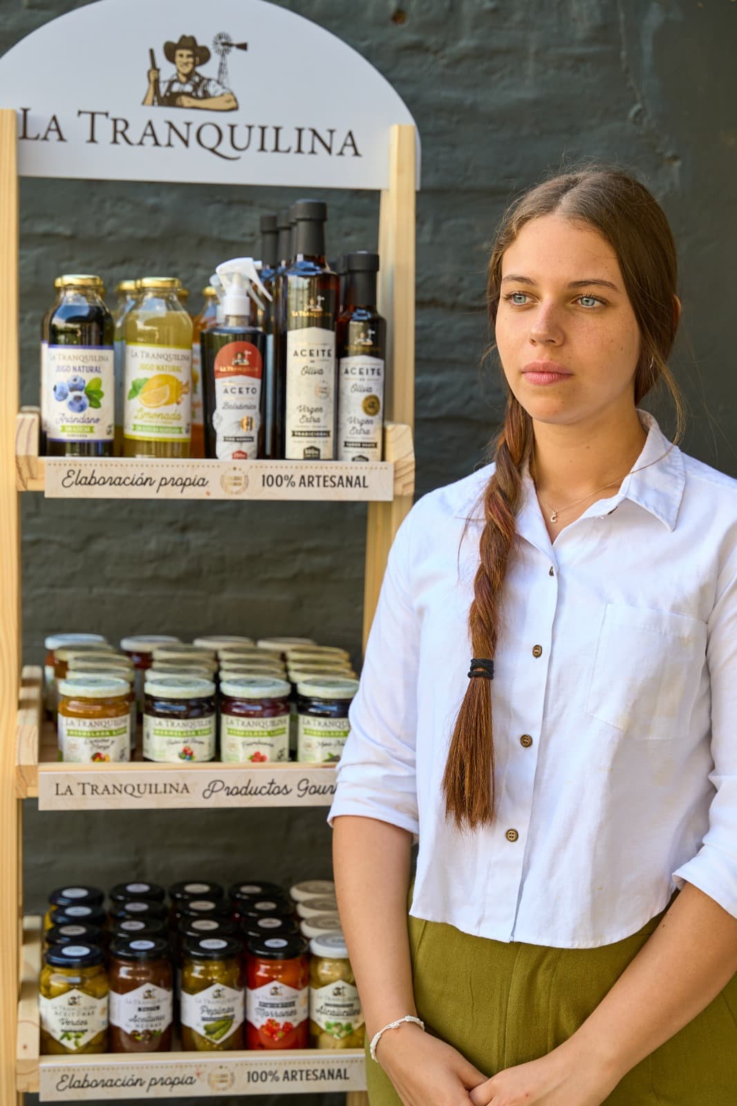 Clarita de pie junto al exhibidor de madera con la línea completa de productos La Tranquilina
